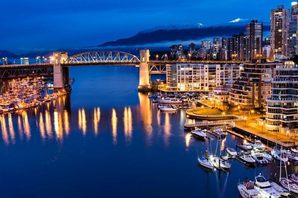 Uma ponte sobre o rio conectando partes da cidade noturna em luzes no fundo de uma montanha em uma névoa branca